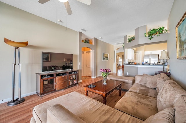 living room featuring a textured ceiling, ceiling fan, a towering ceiling, and light hardwood / wood-style flooring