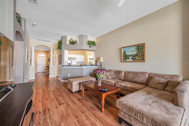 living room featuring a textured ceiling, ceiling fan, light hardwood / wood-style flooring, and decorative columns