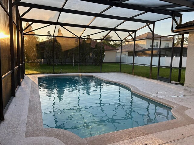 pool at dusk with glass enclosure, a fenced in pool, fence, a yard, and a patio area