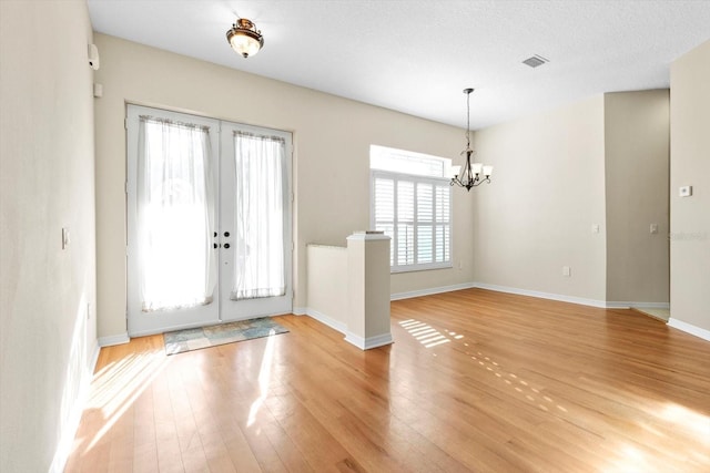 foyer with a notable chandelier, light wood-type flooring, french doors, and a textured ceiling