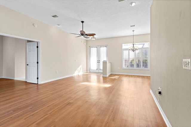 unfurnished living room featuring ceiling fan with notable chandelier, french doors, a textured ceiling, and light wood-type flooring