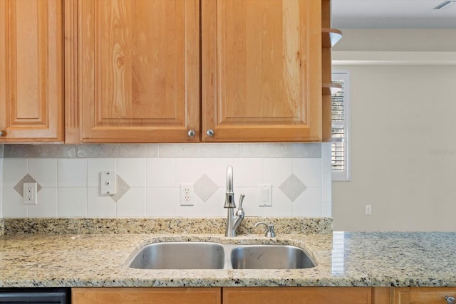 kitchen featuring light stone countertops, tasteful backsplash, and sink