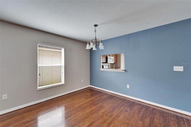 empty room featuring sink, a chandelier, a textured ceiling, and wood-type flooring