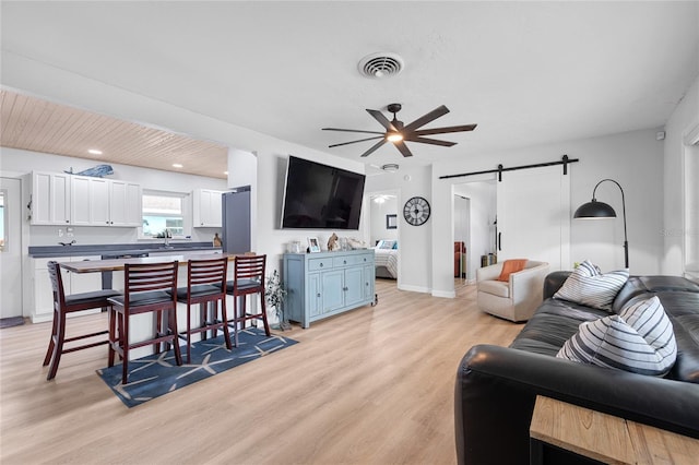 living room with light hardwood / wood-style floors, ceiling fan, and a barn door