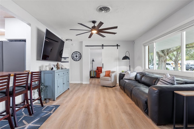 living room with ceiling fan, light hardwood / wood-style floors, and a barn door