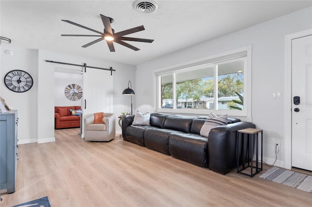 living room with ceiling fan, a barn door, and light wood-type flooring