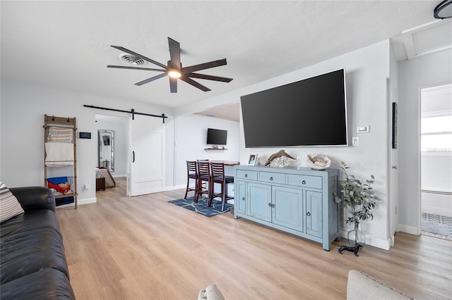 living room with ceiling fan, a barn door, and light hardwood / wood-style floors