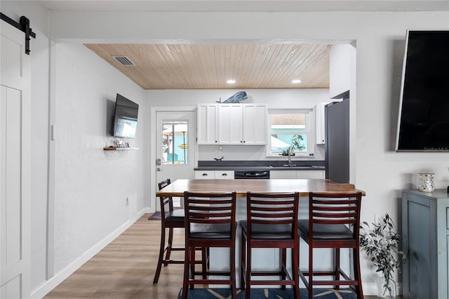 kitchen featuring white cabinets, a barn door, a breakfast bar, and wood ceiling