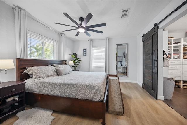 bedroom with ceiling fan, a barn door, a textured ceiling, and light hardwood / wood-style floors