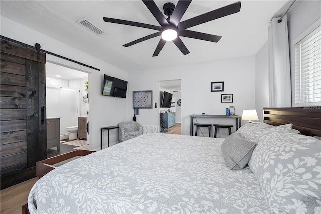 bedroom featuring ceiling fan, ensuite bathroom, a barn door, and hardwood / wood-style flooring