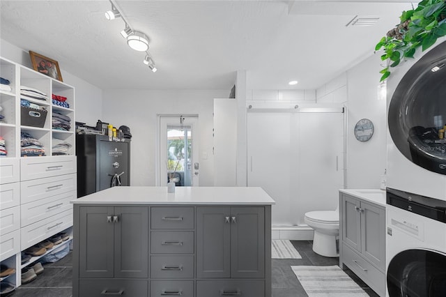 bathroom with toilet, vanity, stacked washer and clothes dryer, a textured ceiling, and a shower with door