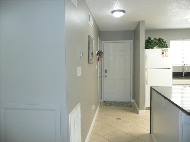 entryway featuring sink, light tile patterned floors, and a textured ceiling