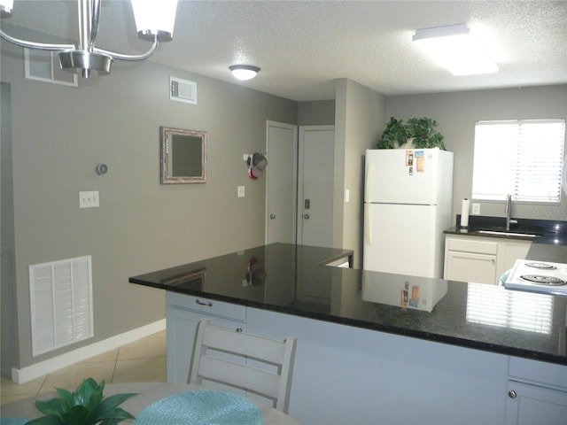 kitchen with light tile patterned flooring, a textured ceiling, white refrigerator, pendant lighting, and white cabinets