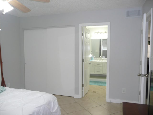 bedroom featuring a textured ceiling, ensuite bathroom, sink, ceiling fan, and light tile patterned floors