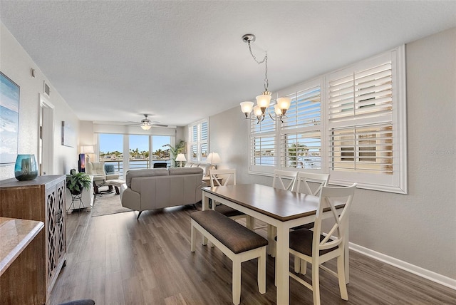 dining space featuring dark wood-type flooring, ceiling fan with notable chandelier, and a textured ceiling