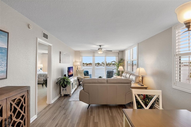 living room with a textured ceiling, ceiling fan, and light hardwood / wood-style flooring