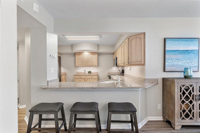 kitchen with light brown cabinetry, a kitchen breakfast bar, kitchen peninsula, and a textured ceiling