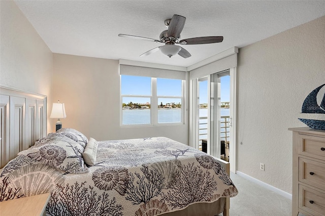 carpeted bedroom featuring a water view, ceiling fan, and access to exterior