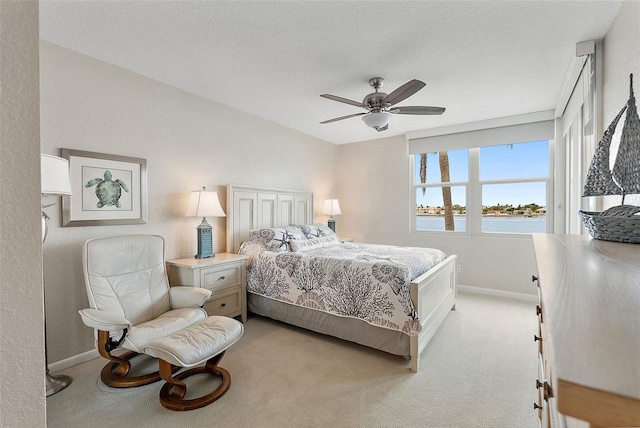 bedroom featuring a textured ceiling, light colored carpet, ceiling fan, and a water view