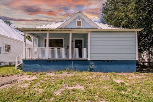 property exterior at dusk with a porch and a lawn