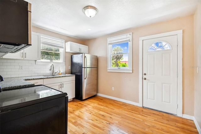 kitchen featuring light stone counters, light hardwood / wood-style floors, decorative backsplash, white cabinetry, and stainless steel refrigerator