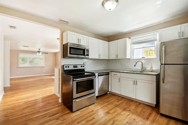 kitchen with appliances with stainless steel finishes, light hardwood / wood-style floors, ceiling fan, white cabinets, and backsplash