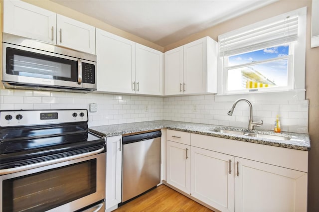 kitchen with stainless steel appliances, light stone countertops, white cabinetry, and sink