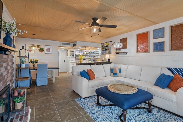 tiled living room with ceiling fan, wooden ceiling, and wooden walls