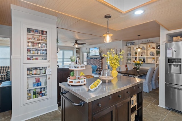 kitchen featuring ceiling fan, stainless steel counters, dark brown cabinetry, hanging light fixtures, and stainless steel fridge with ice dispenser