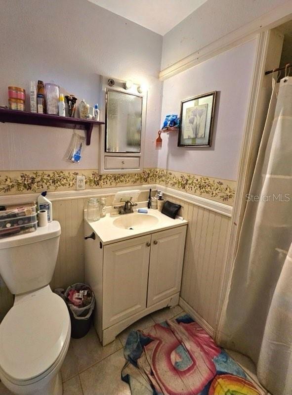 bathroom featuring walk in shower, tile patterned floors, toilet, vanity, and wooden walls