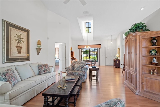 living room with ceiling fan with notable chandelier, light hardwood / wood-style flooring, and high vaulted ceiling