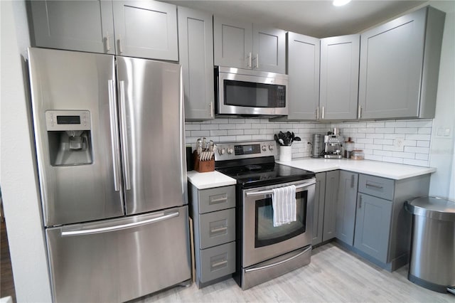 kitchen with stainless steel appliances, decorative backsplash, light wood-type flooring, and gray cabinets