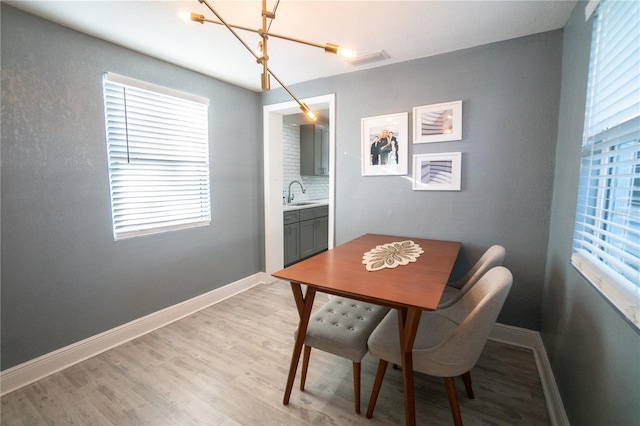 dining room with light wood-type flooring, a notable chandelier, and sink