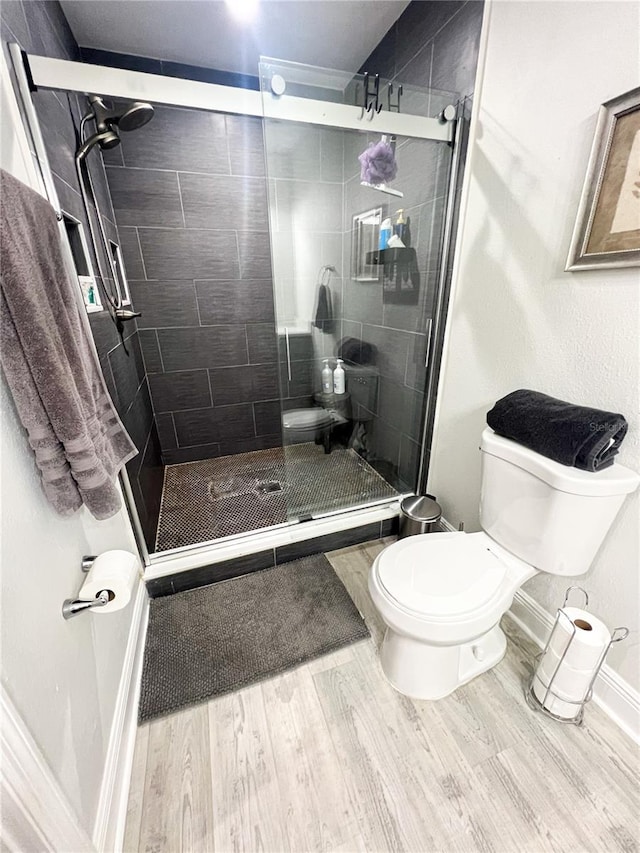 bathroom with toilet, a shower with shower door, and hardwood / wood-style flooring