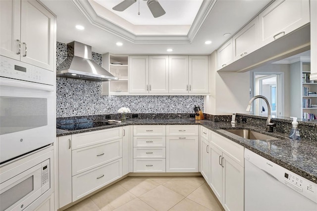 kitchen featuring sink, white cabinetry, wall chimney exhaust hood, white appliances, and dark stone countertops