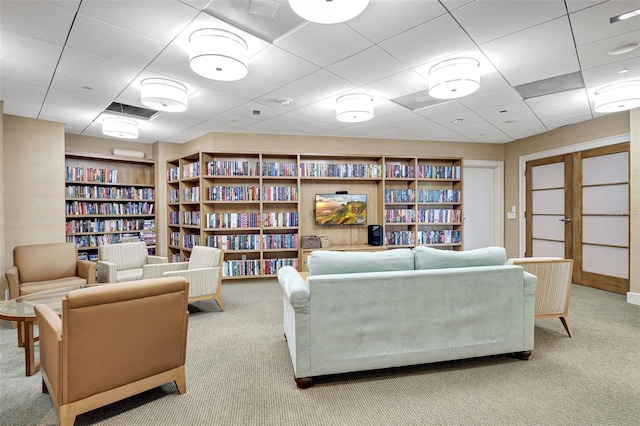 sitting room with built in shelves, a drop ceiling, and light carpet