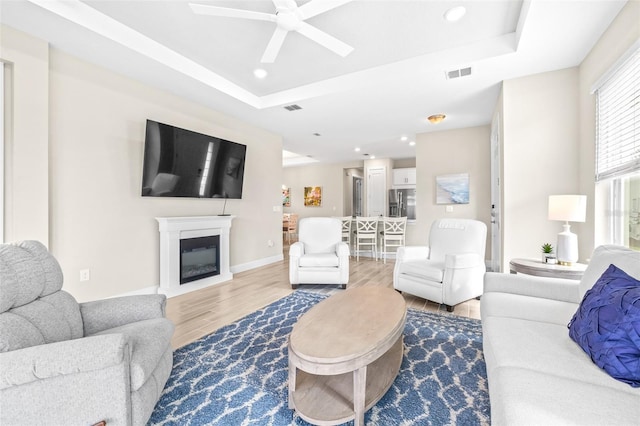 living room featuring ceiling fan, a tray ceiling, and wood-type flooring