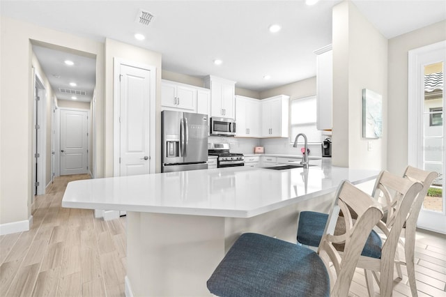 kitchen featuring stainless steel appliances, kitchen peninsula, a kitchen bar, sink, and white cabinetry