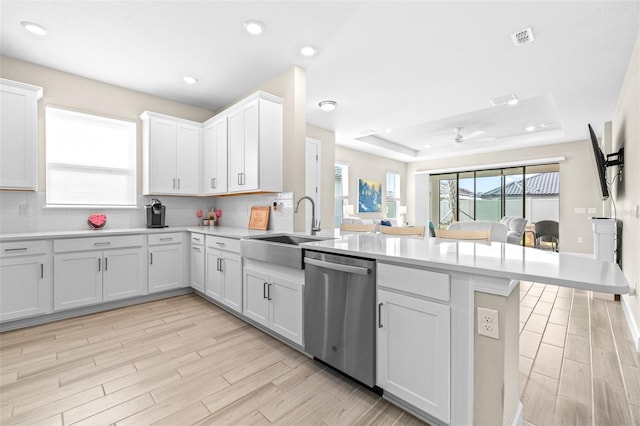 kitchen with kitchen peninsula, a raised ceiling, dishwasher, and white cabinetry