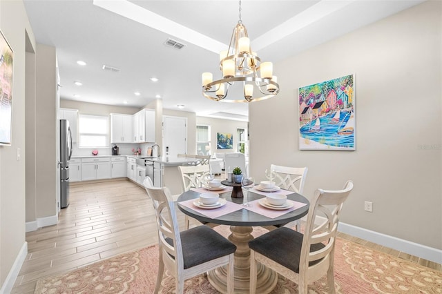 dining space featuring a tray ceiling, light wood-type flooring, and an inviting chandelier