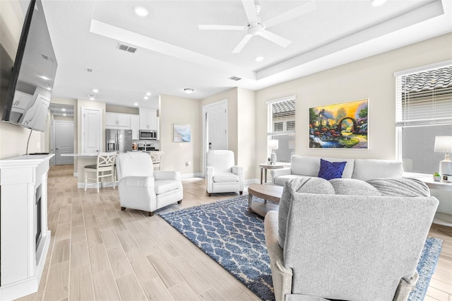 living room featuring a tray ceiling, ceiling fan, and light wood-type flooring