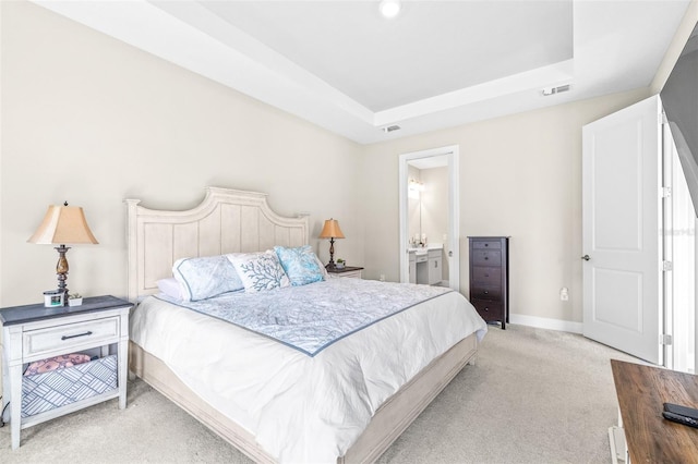 bedroom featuring a tray ceiling, light colored carpet, and ensuite bath