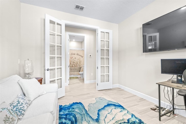 living room featuring french doors, a textured ceiling, and light hardwood / wood-style flooring