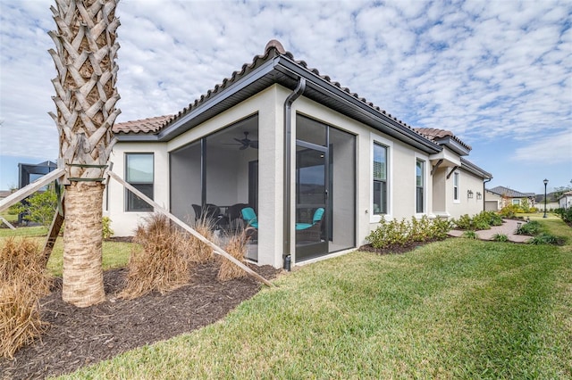 view of side of home featuring a lawn, ceiling fan, and a sunroom