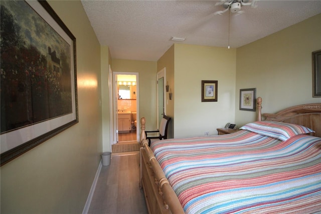 bedroom with a textured ceiling, ceiling fan, connected bathroom, and hardwood / wood-style flooring