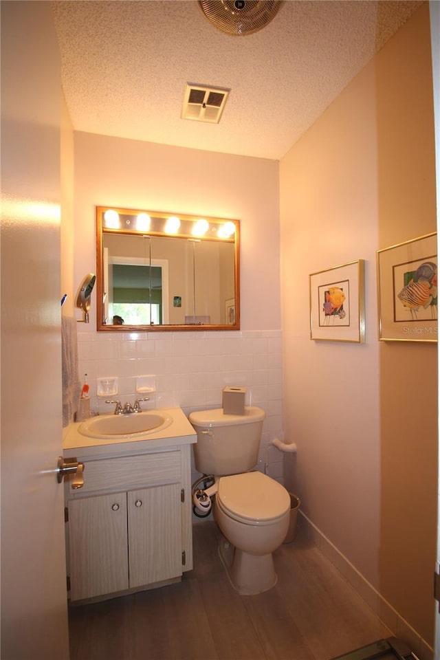 bathroom featuring a textured ceiling, vanity, tile walls, toilet, and hardwood / wood-style flooring