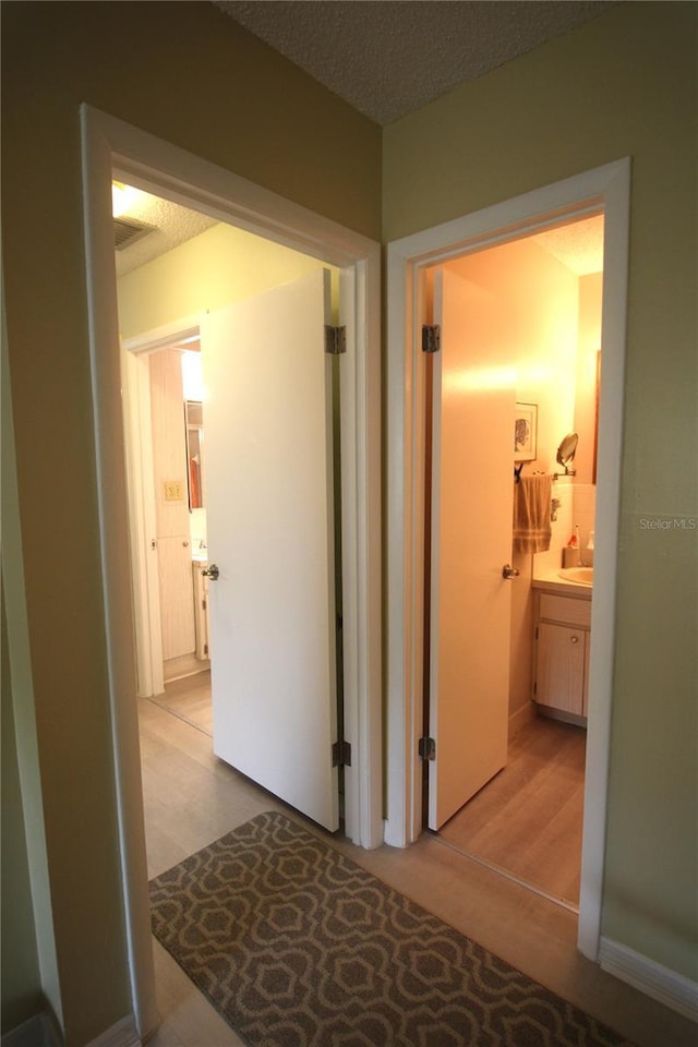 hall with light wood-type flooring and a textured ceiling