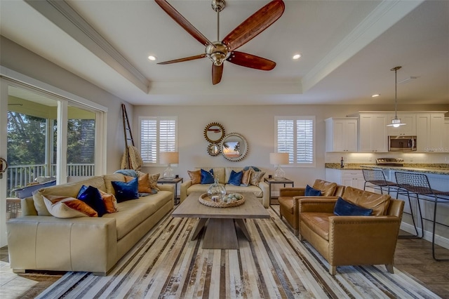 living room featuring ceiling fan, a tray ceiling, ornamental molding, and light hardwood / wood-style flooring