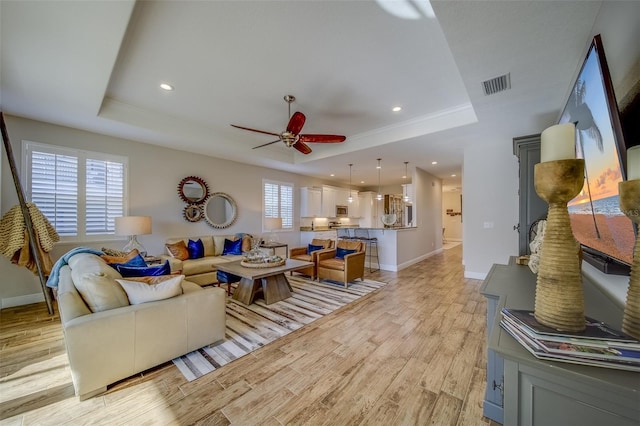 living room featuring a raised ceiling, ceiling fan, light hardwood / wood-style flooring, and a healthy amount of sunlight