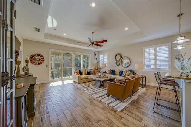 living room with ceiling fan, light wood-type flooring, and a tray ceiling